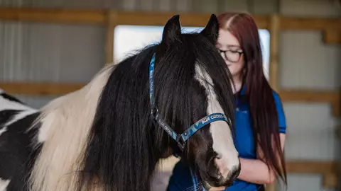 Black and white pony Bandit is held by a teenage girl with long red hair